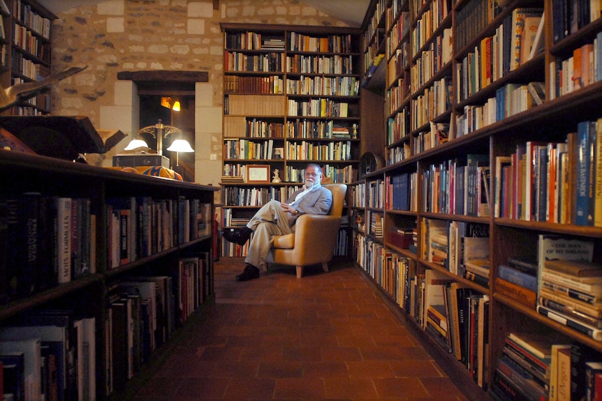Alberto Manguel sits in a chair in his library.