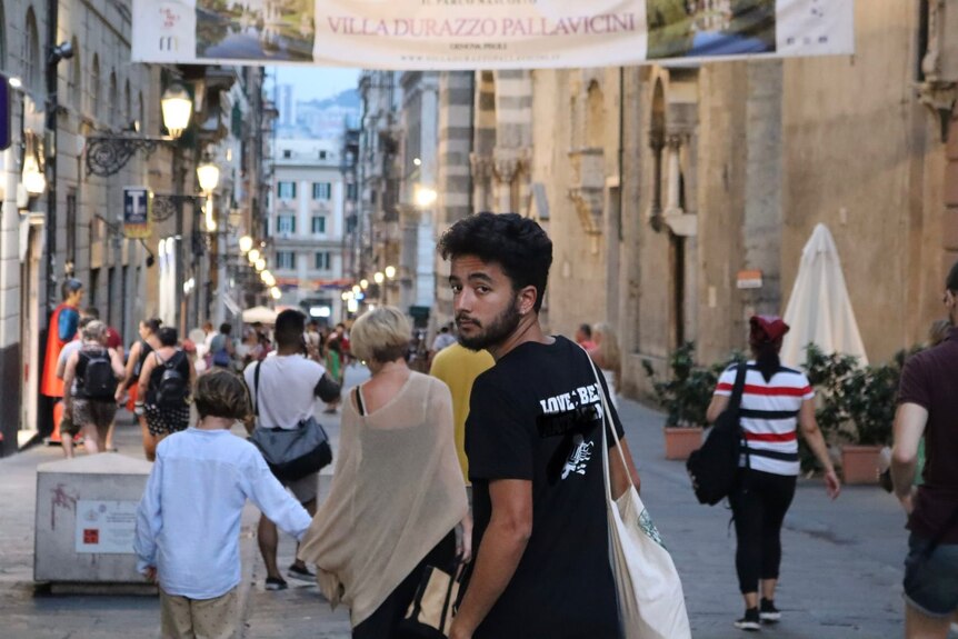 Man in a black shirt with a tote bag, walking through a busy street.
