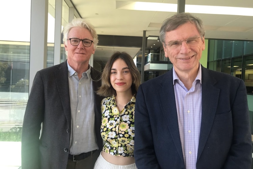 A young woman standing between two older men. All are smiling