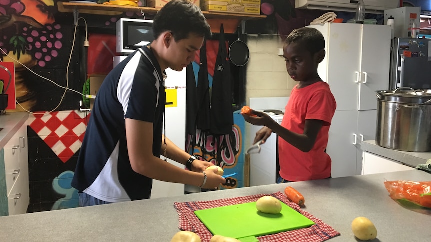 Kids chop vegetables in a kitchen.