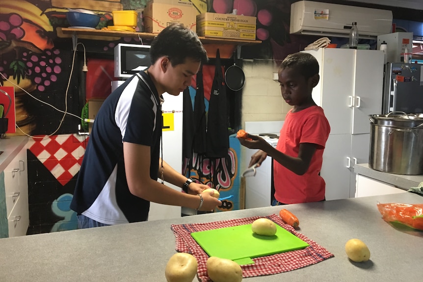 Kids chop vegetables in a kitchen.