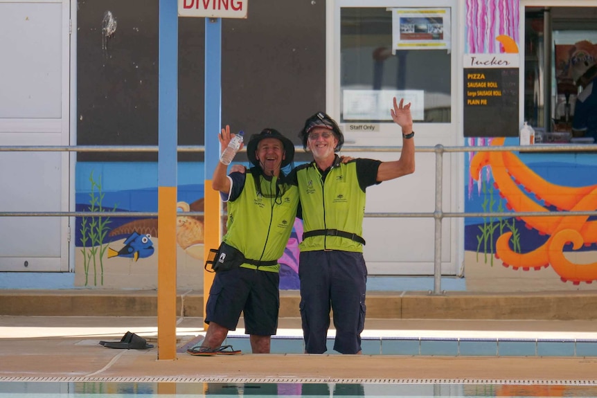 Two men wearing high vis shirts and fly nets smile at a camera.