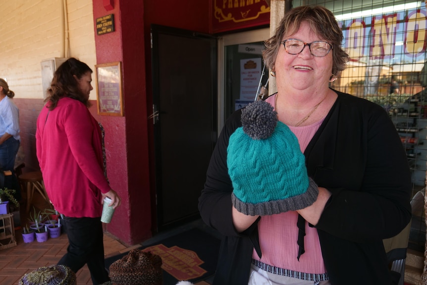 smiling woman holds a hand-made knitted beanie