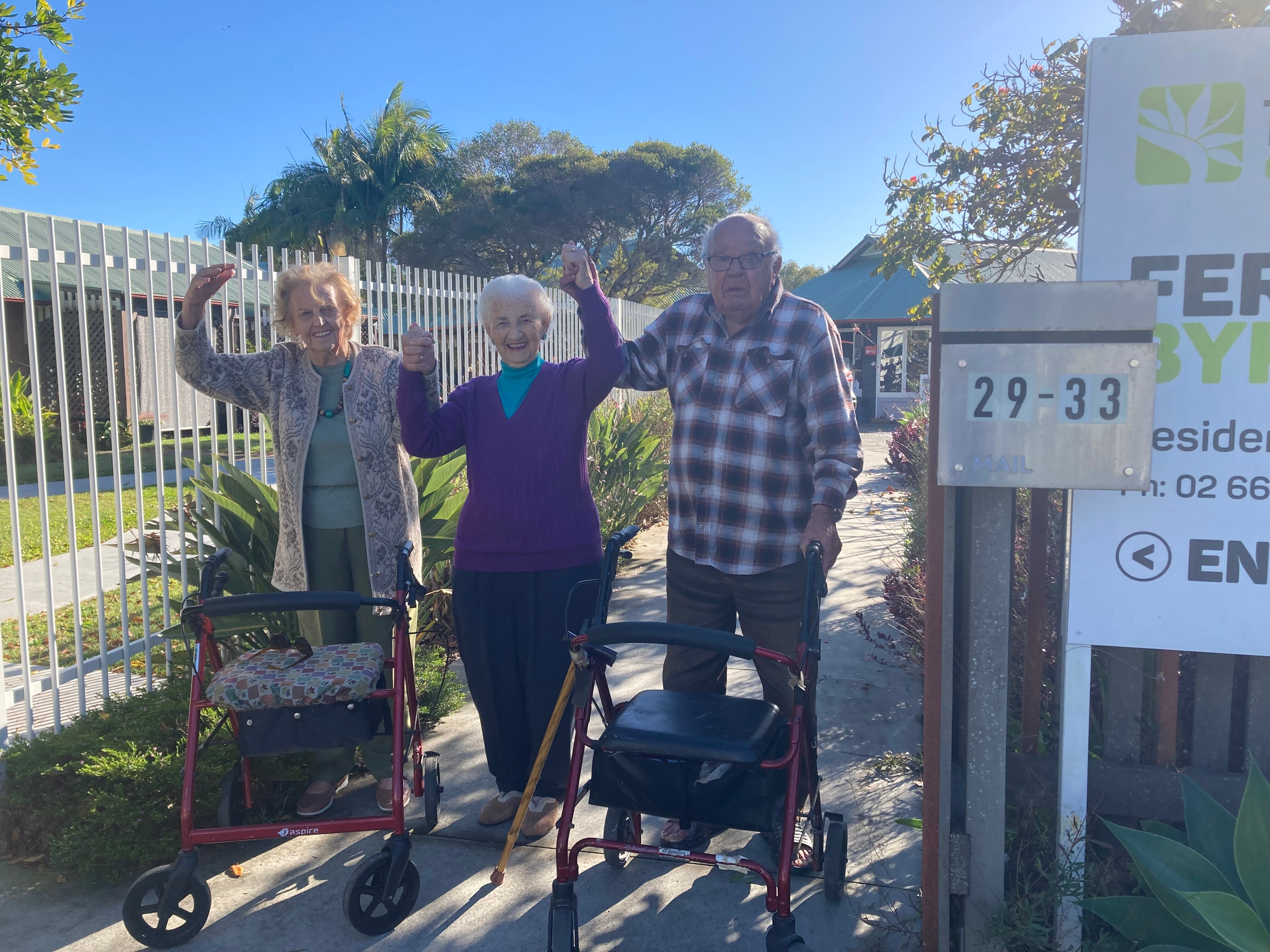 Two elderly women and an elderly man raise their linked hands in celebration.