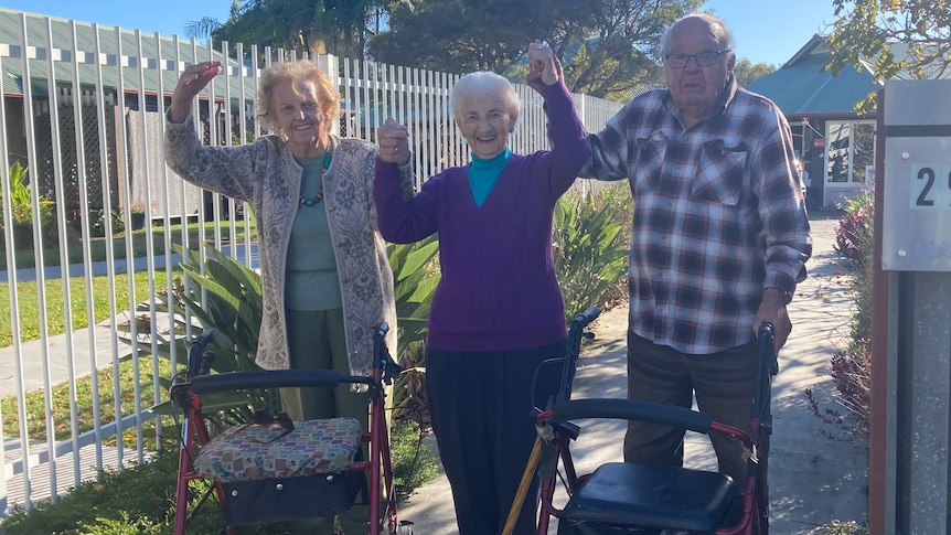 Two elderly women and an elderly man raise their linked hands in celebration.