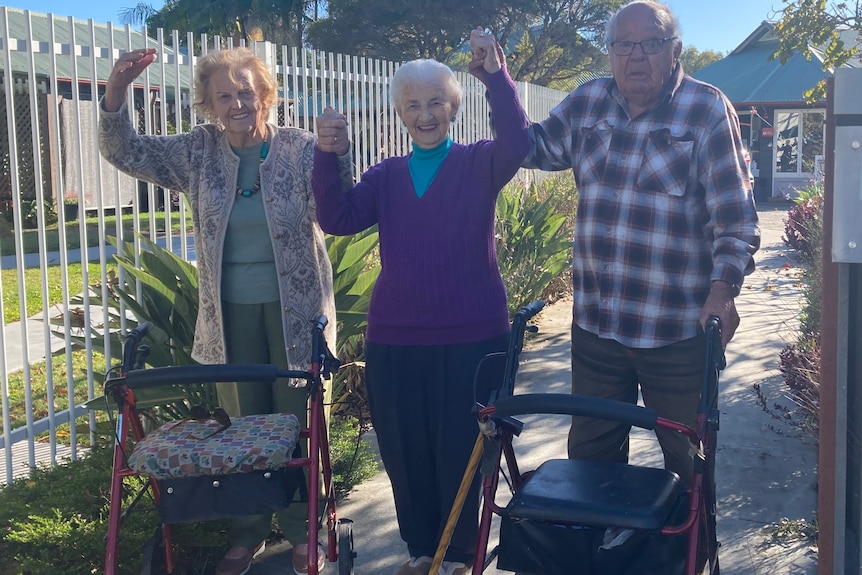 Two elderly women and an elderly man raise their linked hands in celebration.