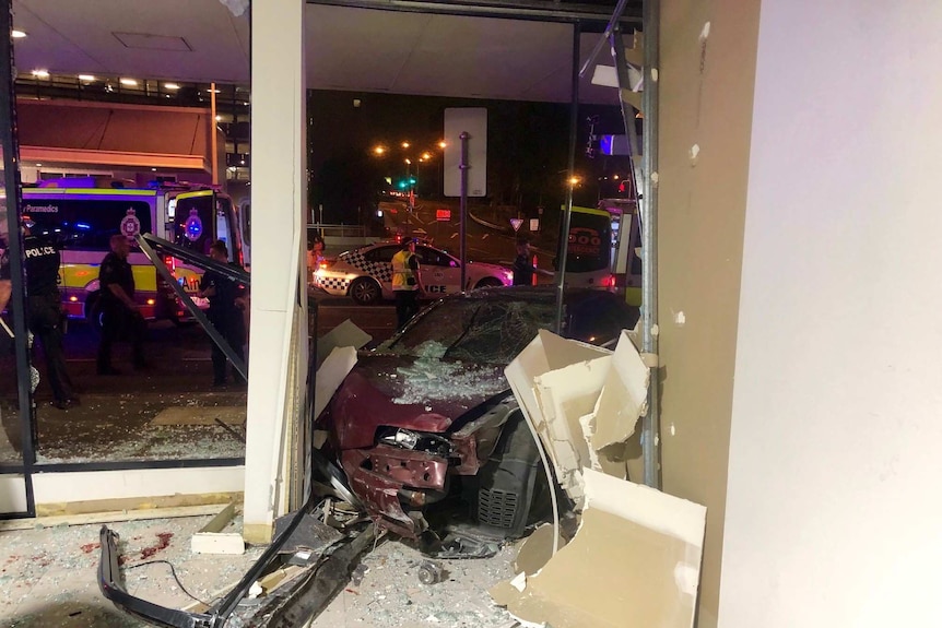 Glass and strewn debris surrounds a car smashed into a Woolloongabba shop.