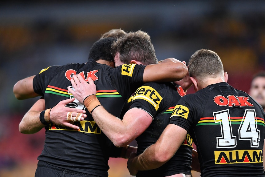A group of Penrith Panthers NRL players have a group hug after the one in the middle (obscured) has scored a try. 