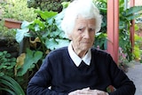 A woman with white hair and a navy jumper sitting in a chair