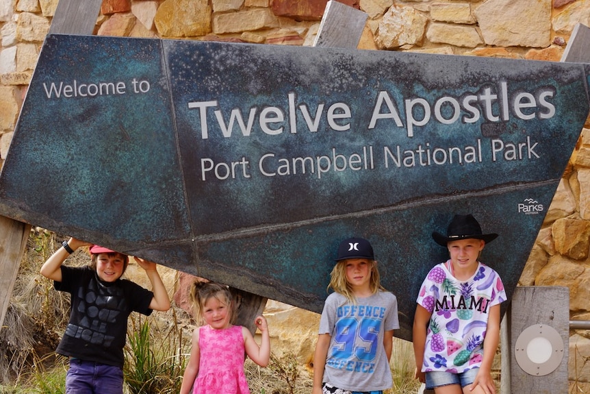 Four children stand in front of a sign reading 'Welcome to the Twelve Apostles'.