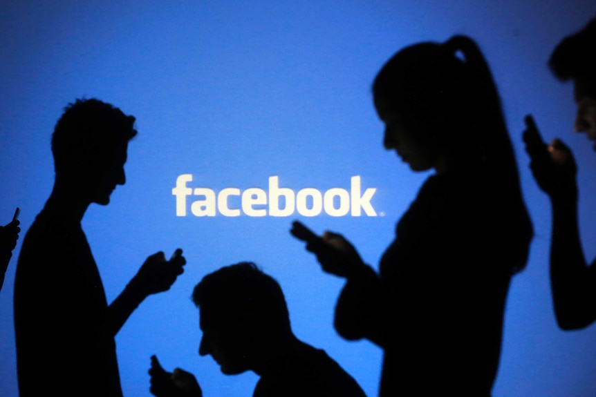 A group of five people silhouetted in front of a blue background with the Facebook logo projected on it.