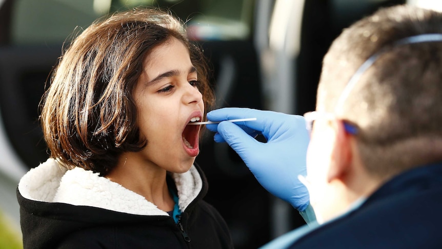 A child getting a test for COVID-19 with a man putting a swab in her mouth.