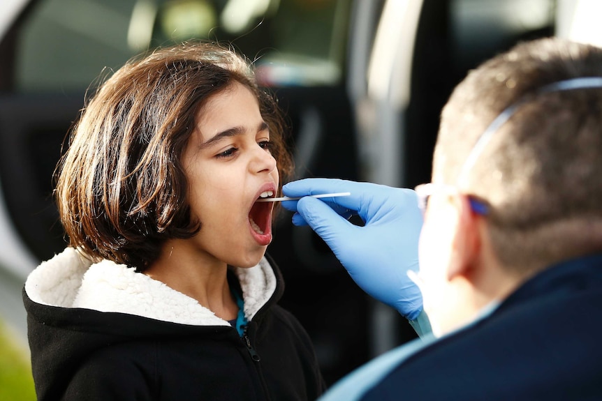 A child getting a test for COVID-19 with a man putting a swab in her mouth.