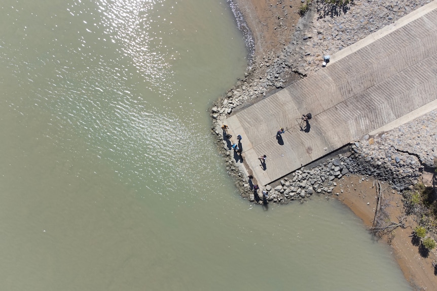 Looking down on people fishing from a boat ramp by a murky creek