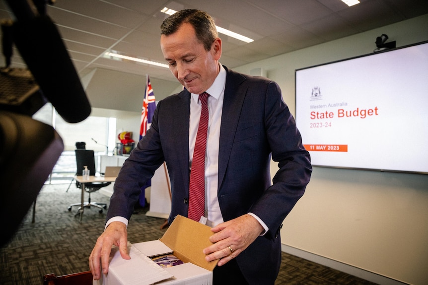 Mark McGowan opens a box of budget documents documents.