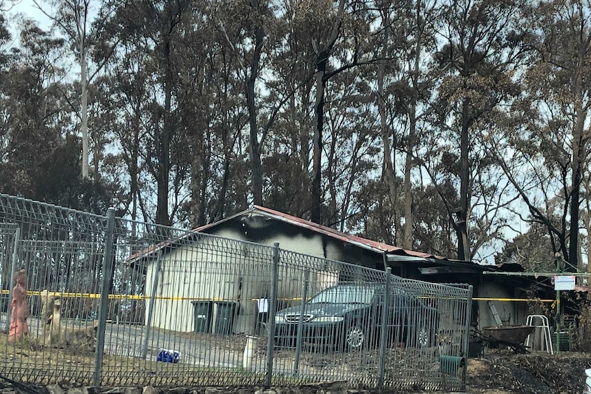 A house amid bushland looks blackened and burnt.