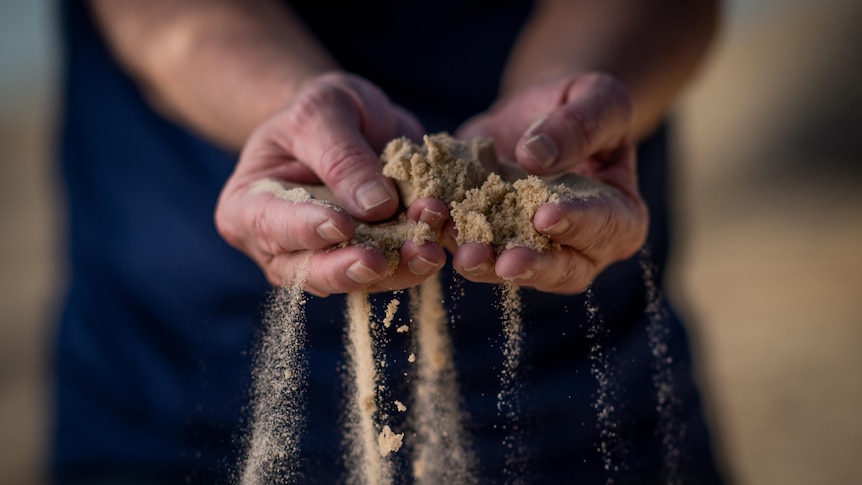 A pair of hands cupping a small amount of sand.