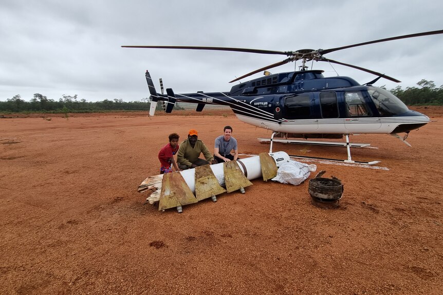 Djawa 'Timmy' Burarrwanga (left), his grandson Dhimurru and Ben Tett with rocket pieces in front of a helicopter.
