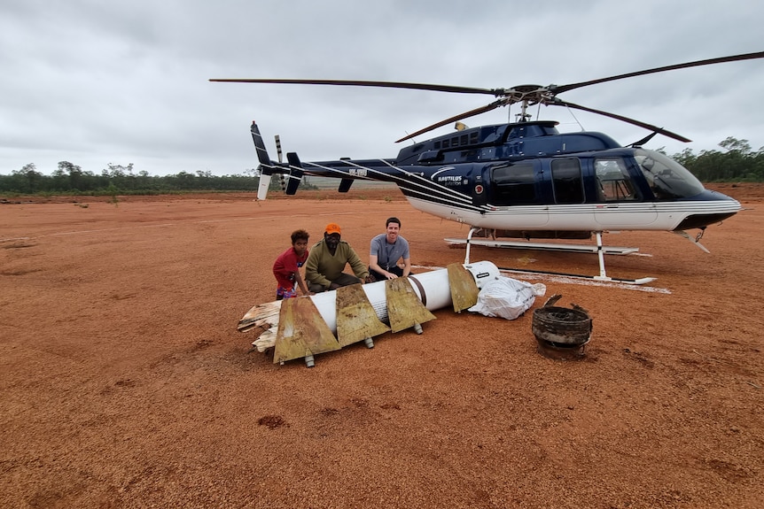 Djawa 'Timmy' Burarrwanga (left), his grandson Dhimurru and Ben Tett with rocket pieces in front of a helicopter.