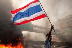 A Red shirt protester carries the Thai flag as tires burn, May 15, 2010 in Bangkok, Thailand (Getty Images: Paula Bronstein)