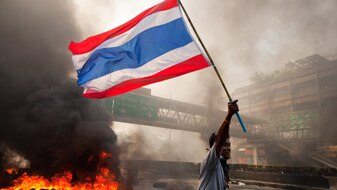 A Red shirt protester carries the Thai flag as tires burn, May 15, 2010 in Bangkok, Thailand (Getty Images: Paula Bronstein)