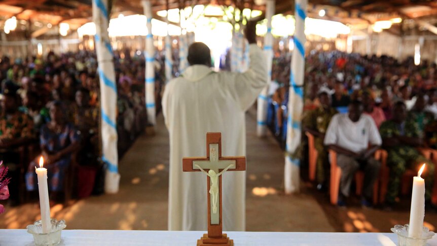 African Catholic Church with priest and followers in background, crucifix in foreground.