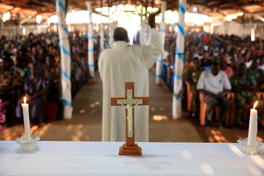 African Catholic Church with priest and followers in background, crucifix in foreground.