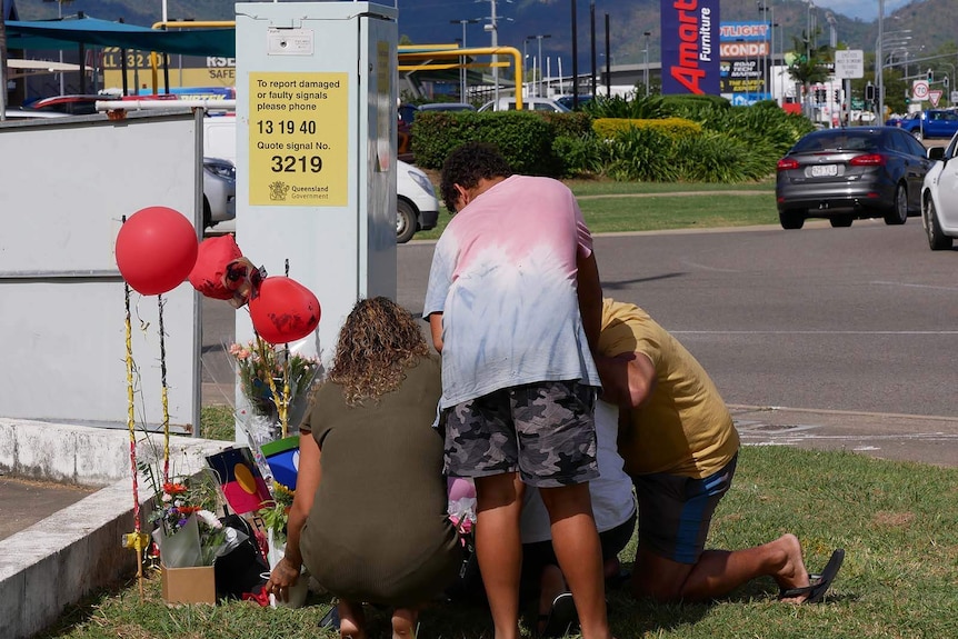 People crouch at a memorial on the side of the road.