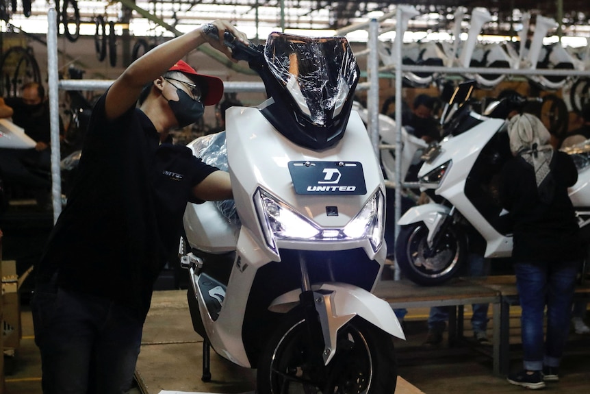 A man assembles an electric motorcycle in a factory setting.