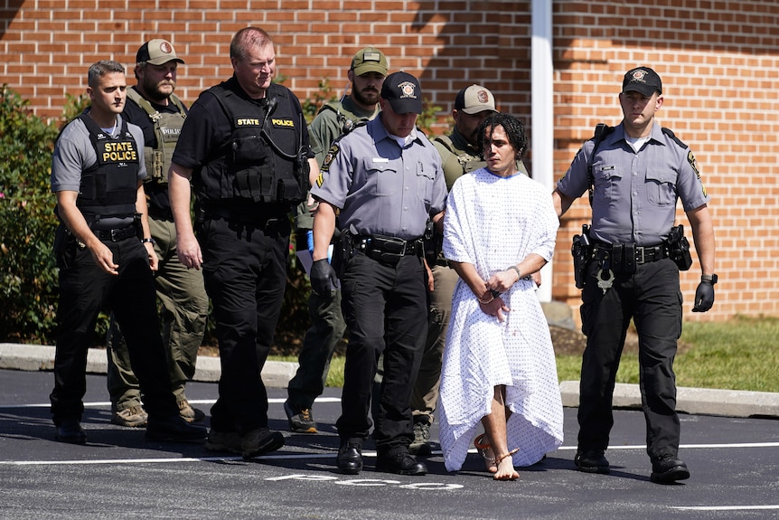 Police escort a prisoner wearing white robe. 