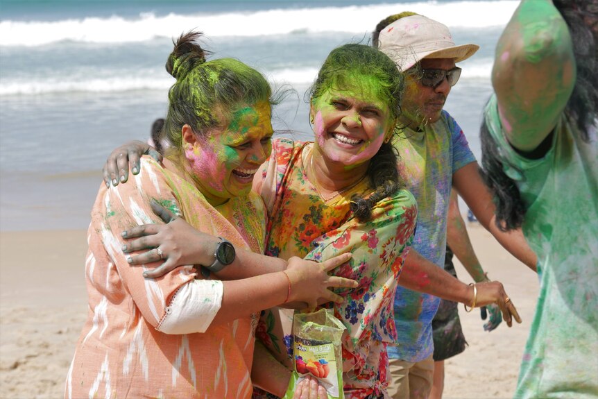 Two women hug and laugh while covered in colourful paint.