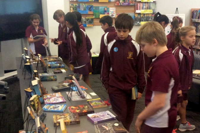 Children look at books on table in school library.