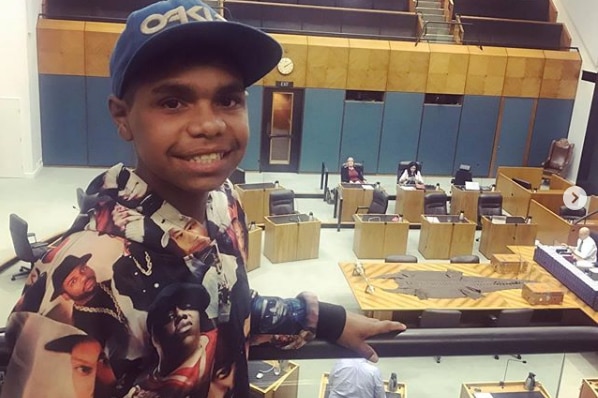 A boy smiling in the balcony of parliament looking down in to the chamber