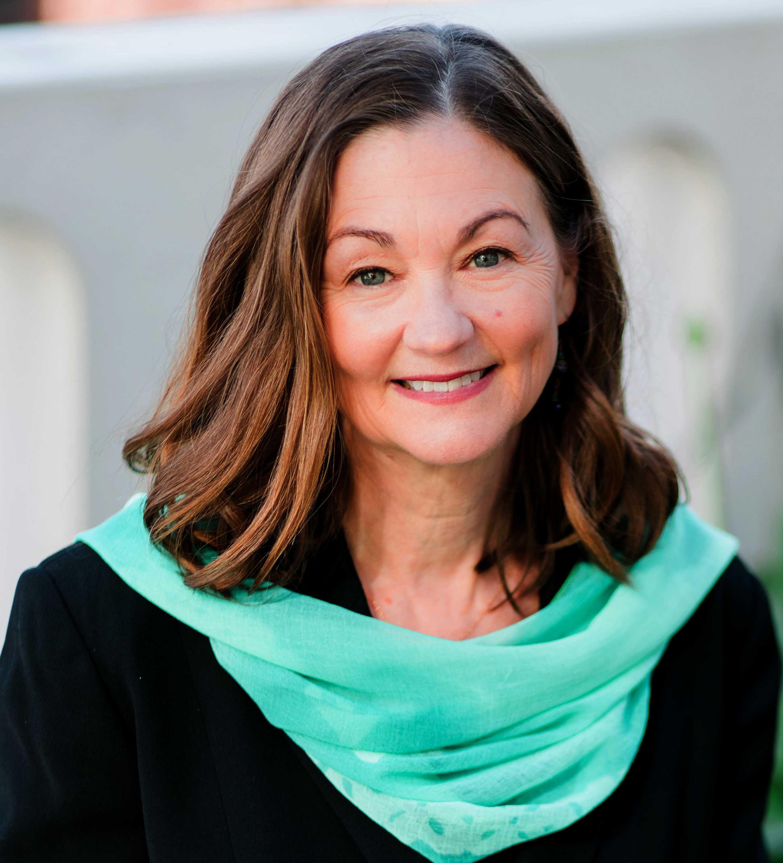 A headshot of Laura Carroll wearing a black top and turquoise scarf.