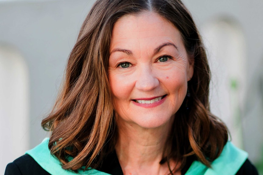 A headshot of Laura Carroll wearing a black top and turquoise scarf.