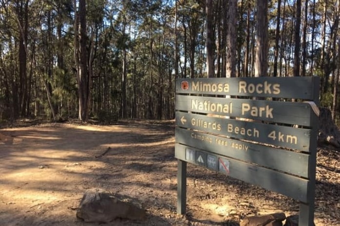 A wooden sign with Mimosa Rocks National Park and walks direction in front of a forest. 