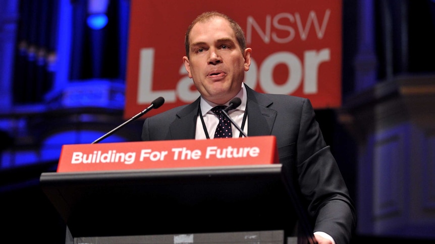 Jamie Clements speaks at a lectern in front of a NSW Labor sign.