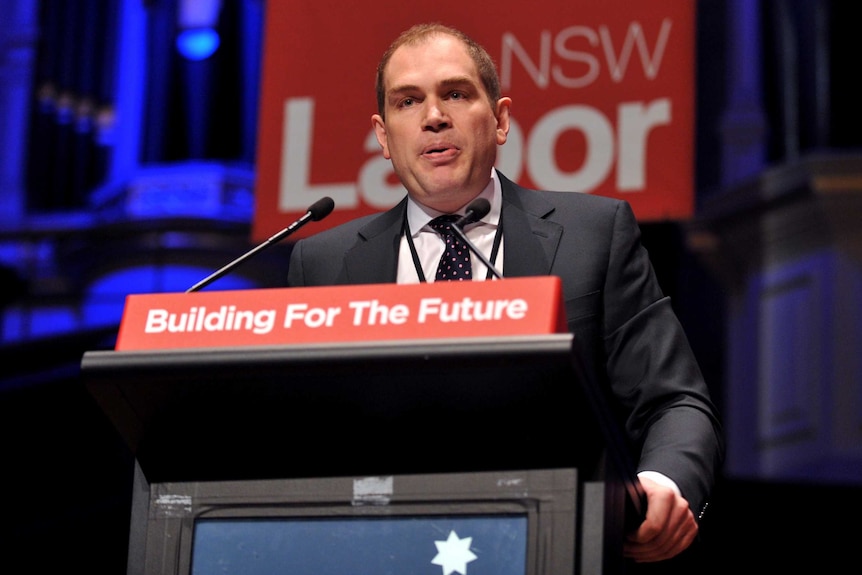 Jamie Clements speaks at a lectern in front of a NSW Labor sign.