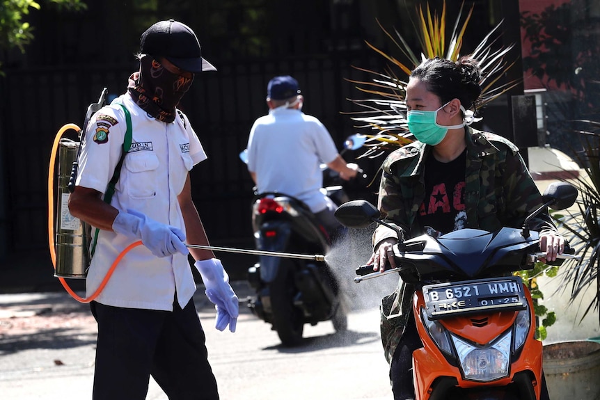 A person on a motorbike is sprayed with disinfectant to help curb the spread of coronavirus in Indonesia.