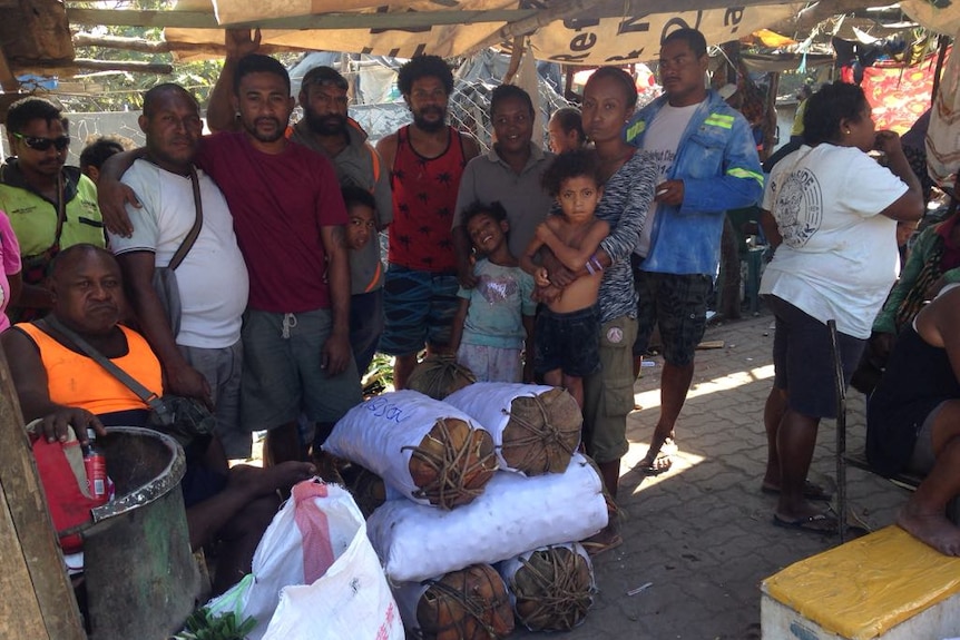 A group of people stand in front of stacks of betel nut in PNG.