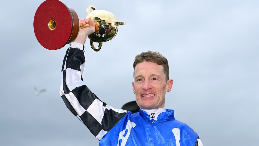 Mark Zahra smiles while holding the Melbourne Cup above his head