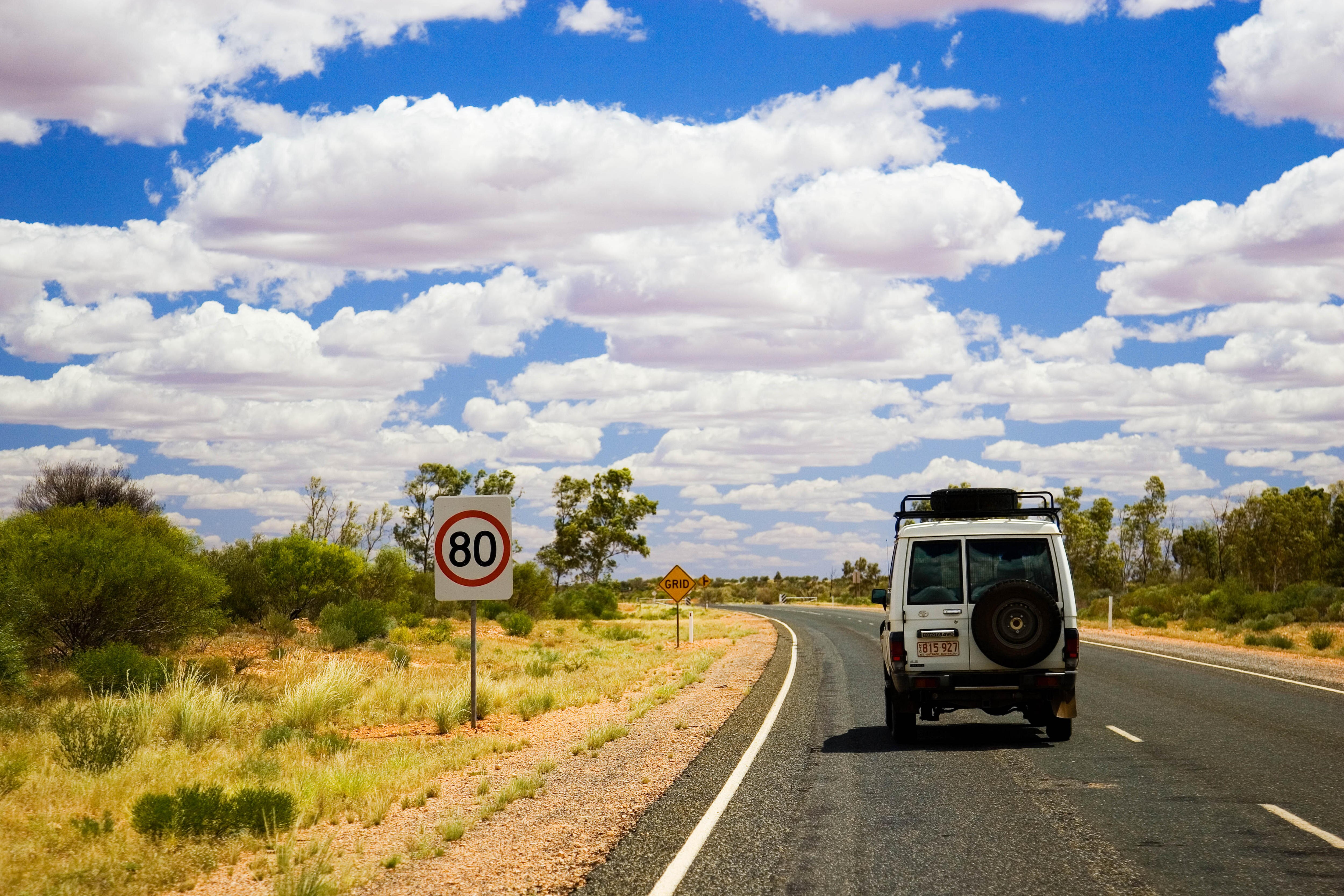 Four wheel drive on a road in the outback with a speed sign in foreground and blue skies