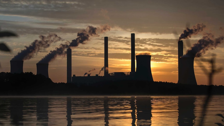 Smoke rises into the air from chimneys in front of an orange sky.