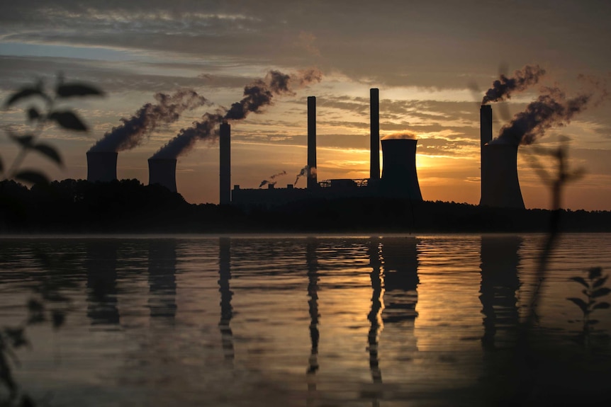 Smoke rises into the air from chimneys in front of an orange sky.