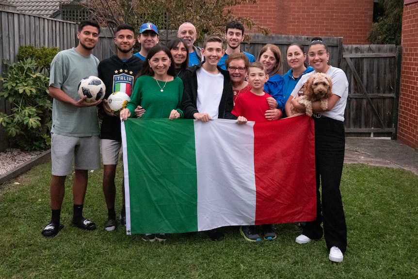 A closeup of 13 Italian supporters, holding a national flag as a family.