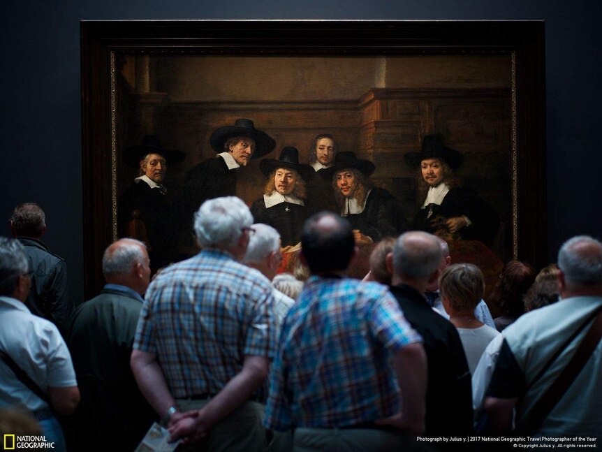 A crowd of spectators stands in front of Rembrandt's masterpiece, Syndics of the Drapers' Guild
