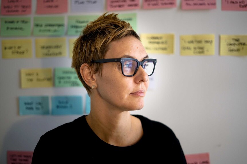 Kristine Rowe sits in front of a wall of post-it notes, and looks off into the distance.