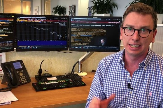 Man in check shirt sits in front of three screens at a Bloomberg terminal.