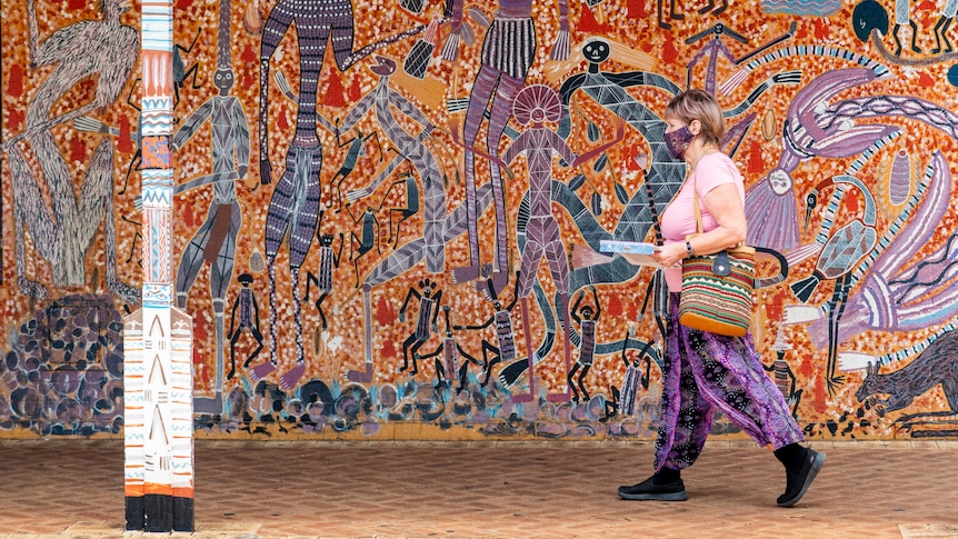 A woman wearing a mask walks past a colourful mural in the town of Katherine.