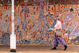 A woman wearing a mask walks past a colourful mural in the town of Katherine.
